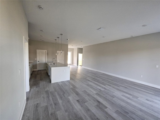 kitchen featuring a kitchen island with sink, sink, wood-type flooring, pendant lighting, and white cabinetry