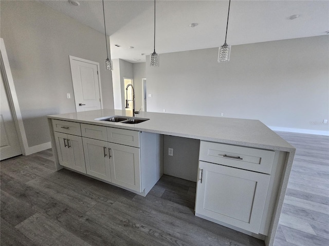 kitchen with hardwood / wood-style floors, sink, hanging light fixtures, and a kitchen island with sink