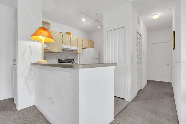 kitchen featuring light colored carpet, white refrigerator, kitchen peninsula, decorative backsplash, and stainless steel range