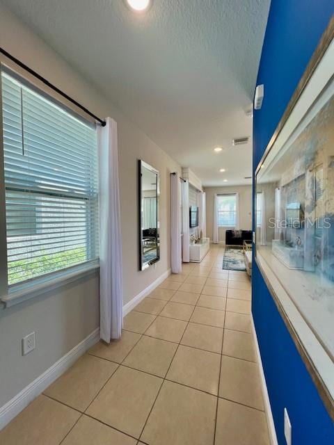 corridor featuring a textured ceiling, a wealth of natural light, and light tile patterned flooring