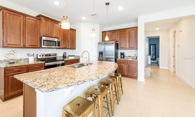 kitchen featuring a breakfast bar area, stainless steel appliances, hanging light fixtures, a sink, and an island with sink