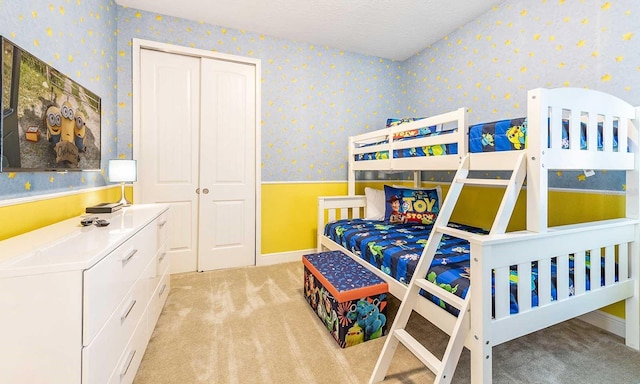 bedroom with a textured ceiling, light colored carpet, baseboards, a closet, and wallpapered walls