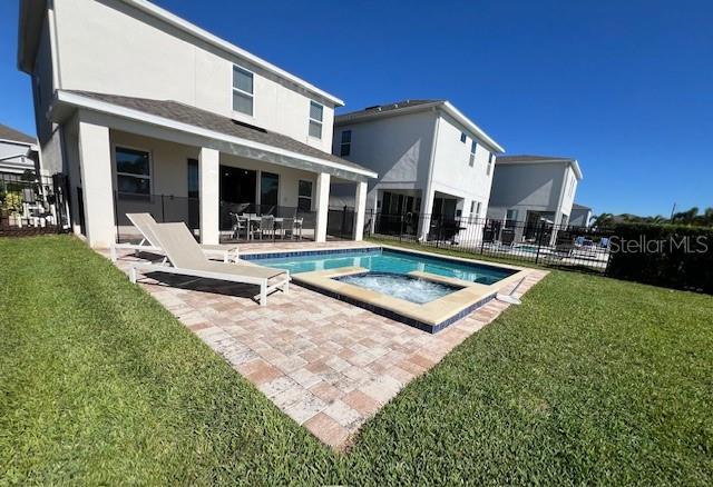 back of house featuring a patio, an in ground hot tub, fence, a lawn, and a fenced in pool