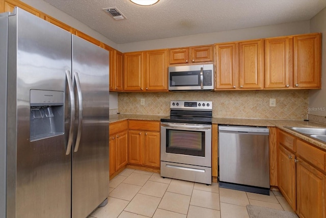 kitchen featuring backsplash, light tile patterned floors, stainless steel appliances, and a textured ceiling