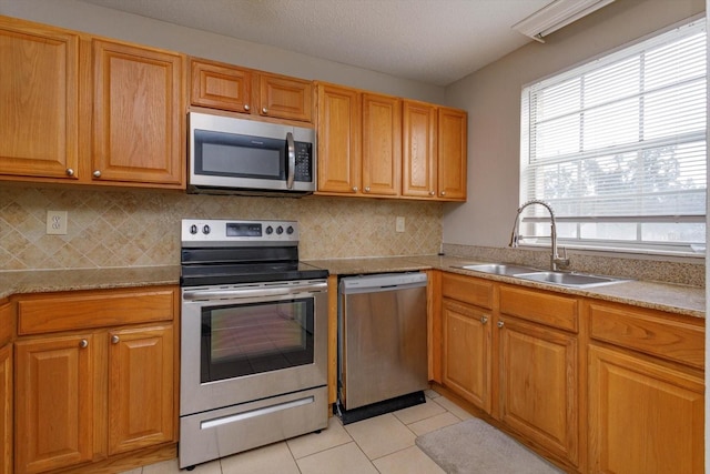 kitchen featuring sink, decorative backsplash, appliances with stainless steel finishes, light tile patterned floors, and a textured ceiling