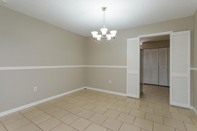 tiled spare room featuring a textured ceiling and a notable chandelier