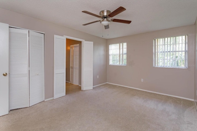 unfurnished bedroom with light carpet, a textured ceiling, multiple windows, and ceiling fan