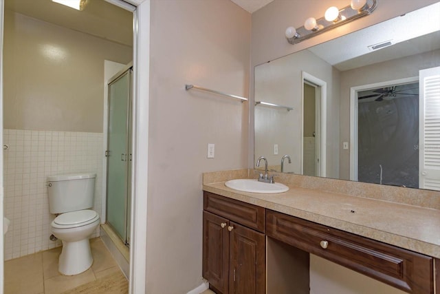 bathroom featuring vanity, a shower with door, tile walls, tile patterned flooring, and toilet