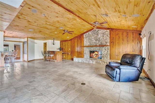 living area featuring a stone fireplace, wooden walls, wood ceiling, and vaulted ceiling