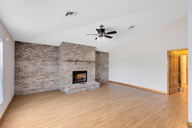 unfurnished living room featuring ceiling fan, brick wall, a brick fireplace, vaulted ceiling, and light wood-type flooring