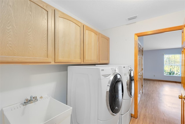 washroom featuring sink, washer and clothes dryer, light hardwood / wood-style floors, and cabinets