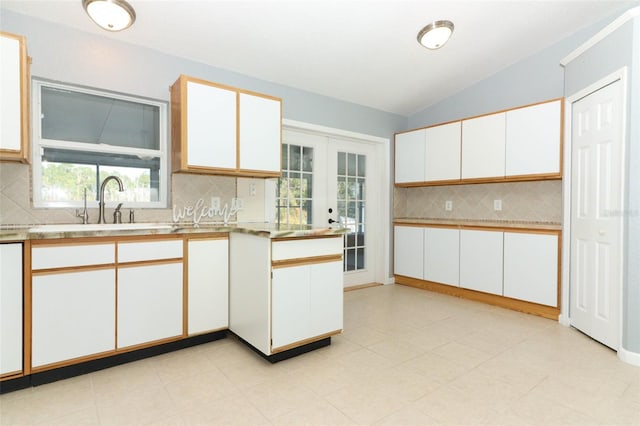 kitchen with tasteful backsplash, french doors, sink, vaulted ceiling, and white cabinets