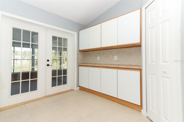 kitchen featuring white cabinetry, french doors, light tile patterned floors, lofted ceiling, and decorative backsplash