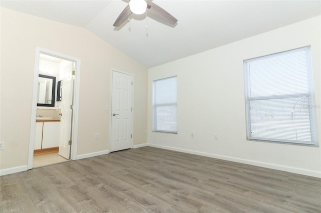 unfurnished bedroom featuring multiple windows, hardwood / wood-style floors, lofted ceiling, and ensuite bath