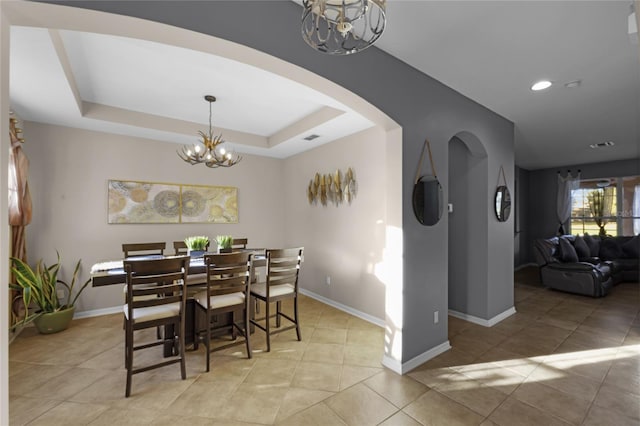 dining space with a notable chandelier, light tile patterned flooring, and a tray ceiling