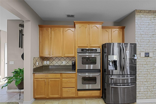 kitchen with a textured ceiling, appliances with stainless steel finishes, light tile patterned flooring, and backsplash