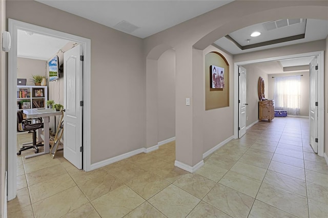 hall featuring light tile patterned floors and a tray ceiling