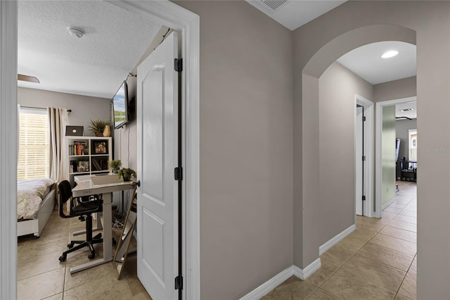 corridor featuring a textured ceiling and light tile patterned floors