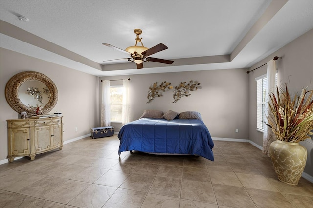 tiled bedroom featuring ceiling fan and a tray ceiling