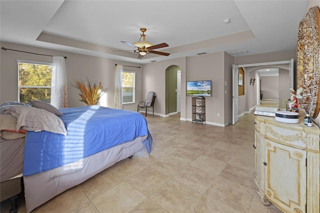 bedroom featuring ceiling fan, a raised ceiling, and light tile patterned floors