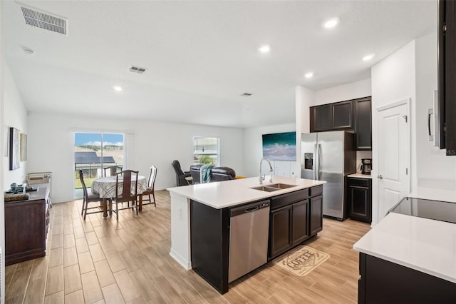 kitchen with appliances with stainless steel finishes, dark brown cabinets, sink, light hardwood / wood-style floors, and a kitchen island with sink