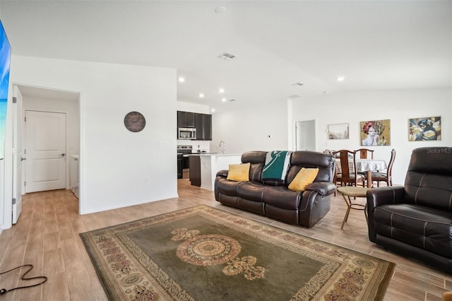 living room featuring light hardwood / wood-style flooring, sink, and vaulted ceiling