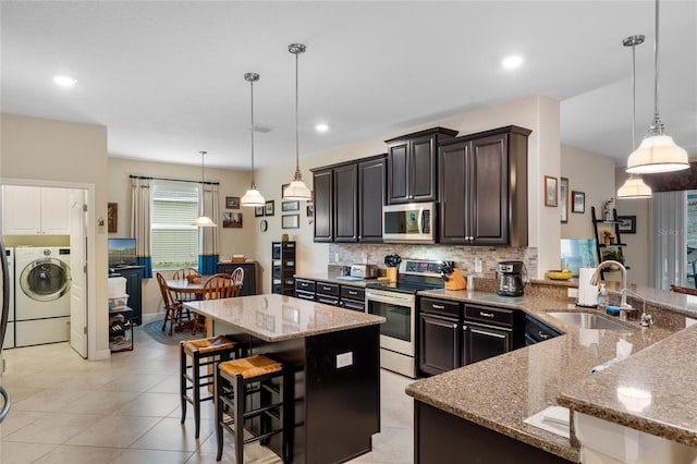 5307 Cortland Dr, Davenport, FL 33837 - kitchen featuring appliances with stainless steel finishes, washer / clothes dryer, light stone countertops, tasteful backsplash, and a breakfast bar