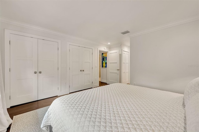 bedroom featuring dark hardwood / wood-style floors, ornamental molding, and two closets