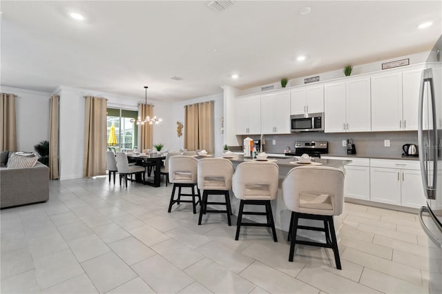 kitchen with white cabinetry, hanging light fixtures, stainless steel appliances, backsplash, and a center island with sink