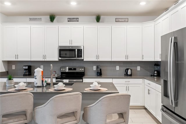 kitchen with stainless steel appliances, white cabinetry, tasteful backsplash, and a breakfast bar area