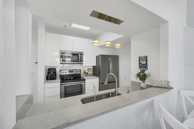 kitchen with light stone countertops, white cabinetry, hanging light fixtures, stainless steel appliances, and kitchen peninsula