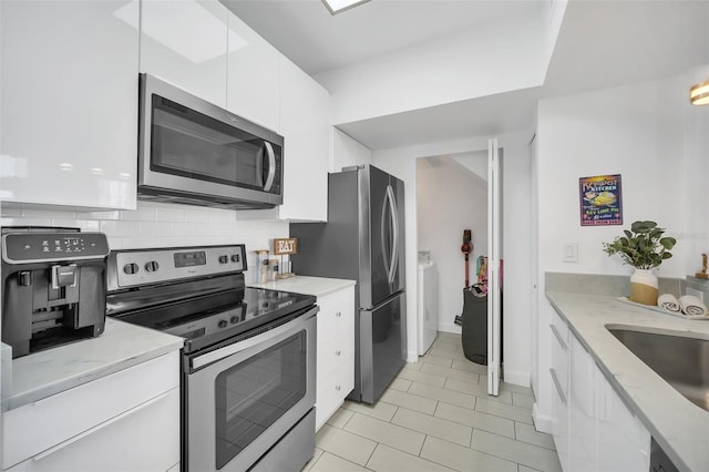 kitchen featuring appliances with stainless steel finishes, tasteful backsplash, sink, independent washer and dryer, and white cabinetry