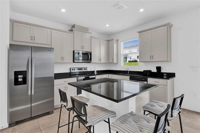 kitchen featuring sink, appliances with stainless steel finishes, a kitchen breakfast bar, light tile patterned floors, and a center island