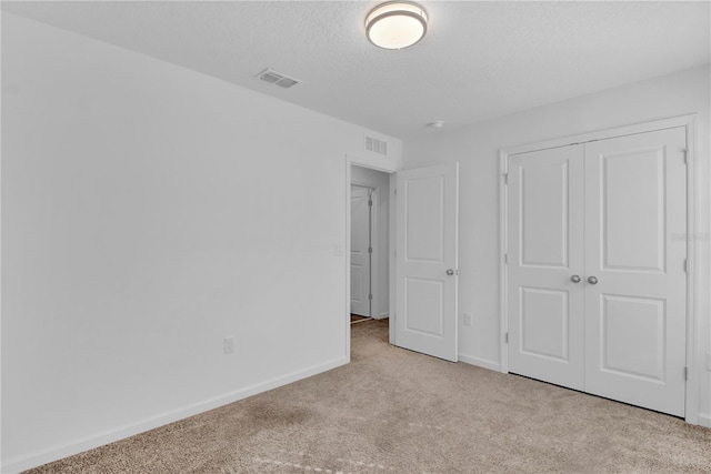 unfurnished bedroom with light colored carpet, a textured ceiling, and a closet