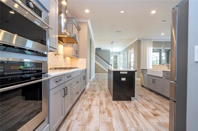 kitchen with decorative light fixtures, a kitchen island, wall chimney exhaust hood, and light hardwood / wood-style floors