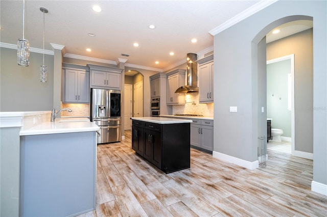 kitchen with tasteful backsplash, stainless steel appliances, wall chimney range hood, decorative light fixtures, and light hardwood / wood-style floors