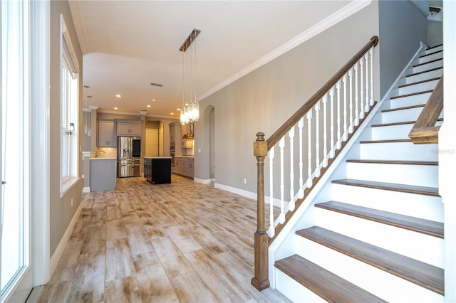 stairway with wood-type flooring, a notable chandelier, and ornamental molding