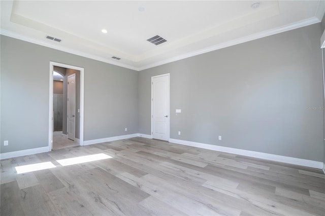 empty room with light hardwood / wood-style floors, a raised ceiling, and crown molding