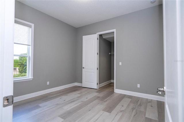 unfurnished bedroom featuring a walk in closet, a textured ceiling, and light hardwood / wood-style floors