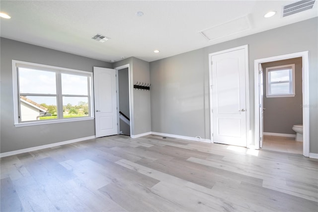 unfurnished bedroom featuring multiple windows, ensuite bathroom, and light wood-type flooring