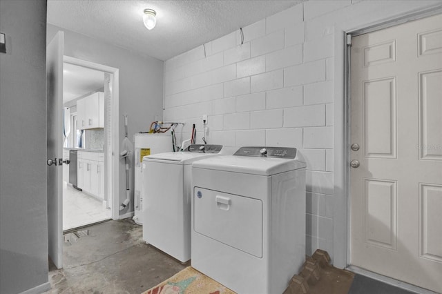 clothes washing area featuring a textured ceiling, washing machine and dryer, and water heater