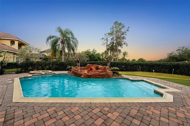 pool at dusk featuring a lawn, pool water feature, and an in ground hot tub