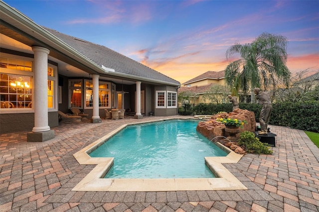 pool at dusk with pool water feature and a patio area