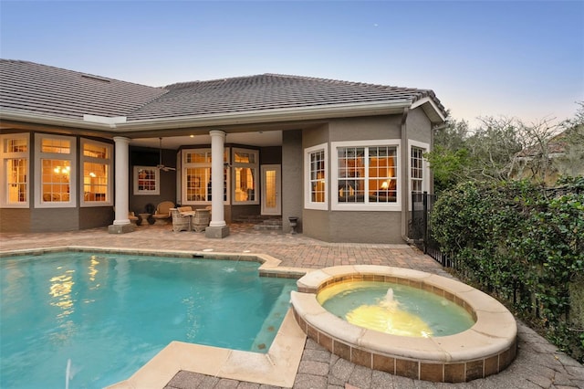 back house at dusk featuring a patio and a pool with hot tub