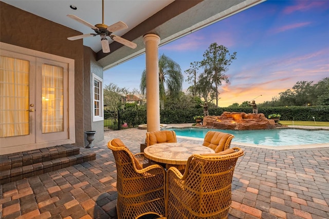 patio terrace at dusk featuring pool water feature, ceiling fan, and a fenced in pool