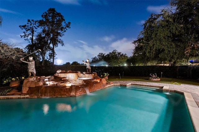 pool at dusk featuring a lawn and pool water feature