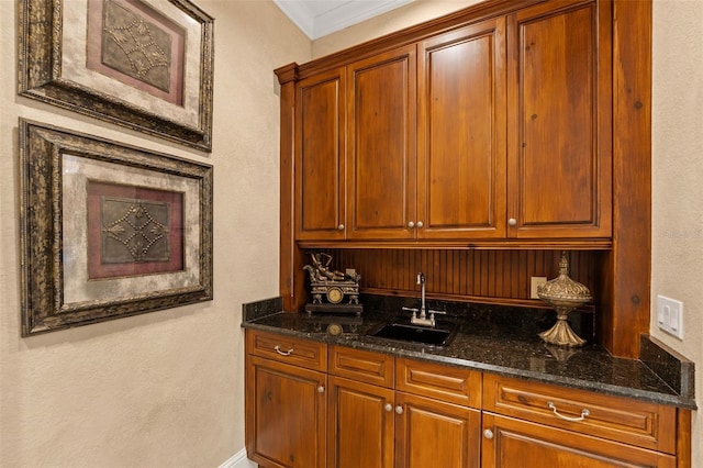 bar with ornamental molding, sink, and dark stone counters