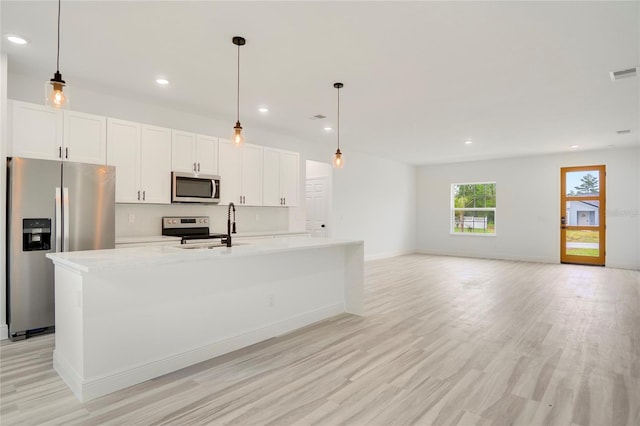 kitchen featuring stainless steel appliances, white cabinetry, an island with sink, and light hardwood / wood-style flooring