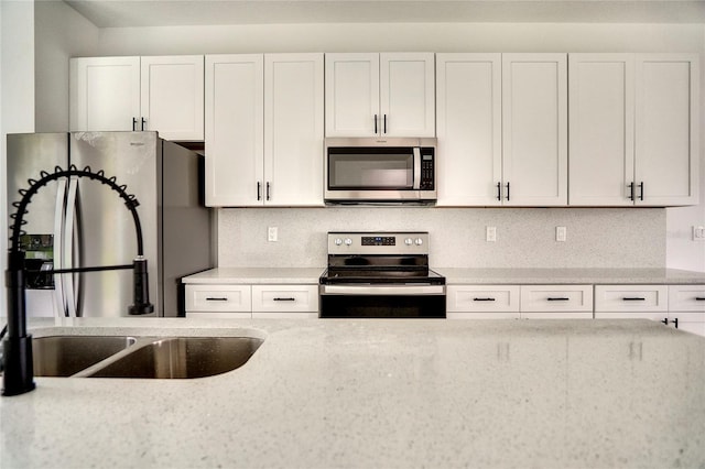 kitchen with white cabinets, sink, backsplash, light stone countertops, and appliances with stainless steel finishes