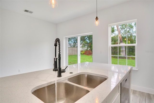 kitchen featuring light stone countertops, pendant lighting, sink, and a healthy amount of sunlight